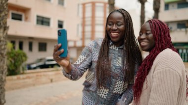 İki Afro-Amerikalı arkadaş gülümsüyor. Parktaki akıllı telefonun yanında özçekim yapıyorlar.