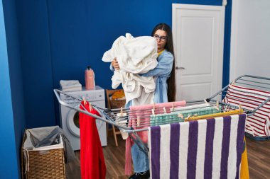 Young hispanic woman hanging clothes on clothesline at laundry room