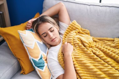 Genç sarışın kadın kanepede uzanıp evde uyuyor.