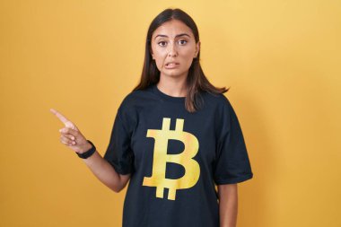 Bitcoin tişörtü giyen genç İspanyol kadın endişeli ve gergin bir şekilde işaret ediyor. 