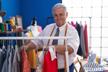 Orta yaşlı, gri saçlı, sırıtan, kendine güvenen, terzi dükkanında kendine güvenen bir adam.