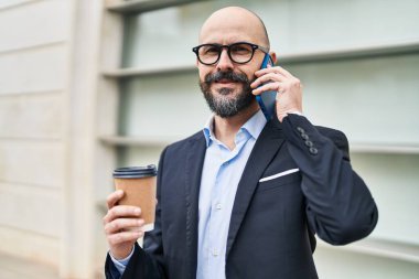 Genç kel iş adamı akıllı telefondan konuşuyor sokakta kahve içiyor.