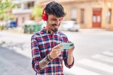 Young hispanic man smiling confident playing video game at street