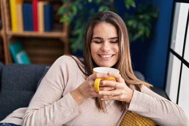 Genç ve güzel İspanyol kadın evdeki kanepede oturup kahve içiyor.