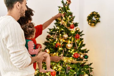 Couple and daughter smiling confident decorating christmas tree at home