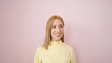 Young blonde woman smiling confident looking to the side over isolated pink background