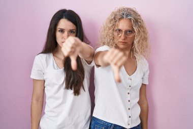 Anne ve kızının pembe arka planda yan yana durması mutsuz ve kızgın görünmeleri reddedilmeleri ve olumsuz davranışlar sergilemeleri. kötü ifade. 