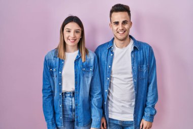 Young hispanic couple standing over pink background with a happy and cool smile on face. lucky person. 