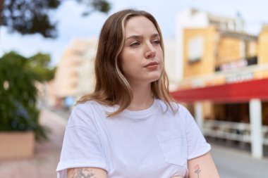 Beyaz bir kadın sokakta ciddi bir ifadeyle yan tarafa bakıyor.