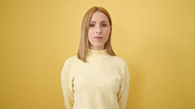 Young blonde woman standing with relaxed expression over isolated yellow background