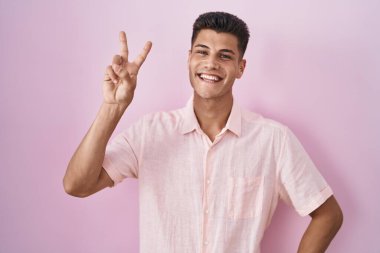 Pembe arka planda duran genç İspanyol adam kameraya bakıp zafer işareti yapıyor. İki numara.. 