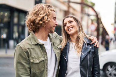 Kadın ve erkek gülümsüyor. Kendilerine güveniyorlar. Sokakta sarılıyorlar.