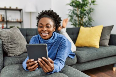 African american woman using touchpad lying on sofa at home