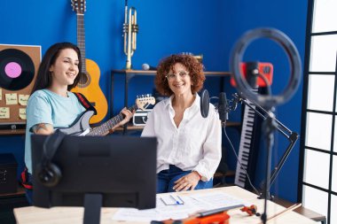 Two women musicians having online electrical guitar lesson by smartphone at music studio