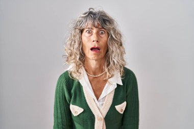 Middle age woman standing over white background in shock face, looking skeptical and sarcastic, surprised with open mouth 