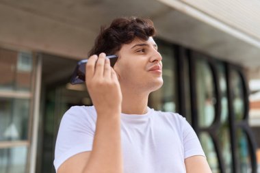 Non binary man smiling confident listening audio message by the smartphone at street