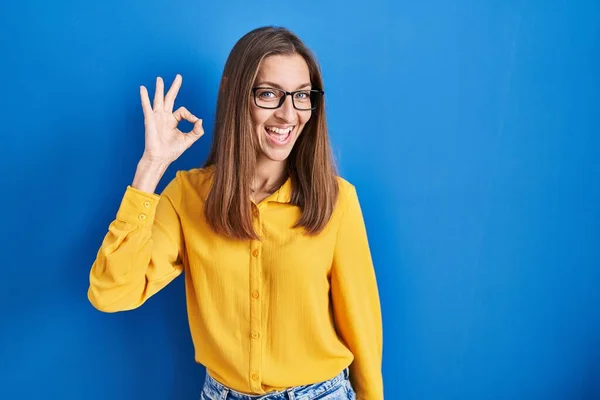 Mujer Joven Con Gafas Pie Sobre Fondo Azul Sonriendo Positiva —  Fotos de Stock