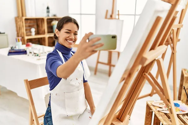 年轻的拉丁女人笑着自信地在艺术工作室的智能手机前自拍 — 图库照片
