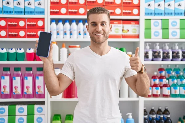 Young Caucasian Man Working Pharmacy Drugstore Showing Smartphone Screen Smiling — Zdjęcie stockowe