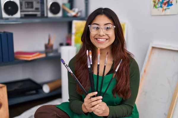 Young Hispanic Woman Artist Holding Paintbrushes Sitting Floor Art Studio — Foto Stock