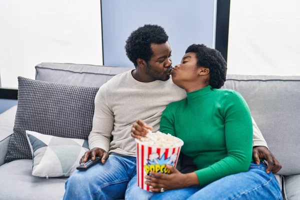 African american man and woman couple watching movie eating popcorn kissing at home