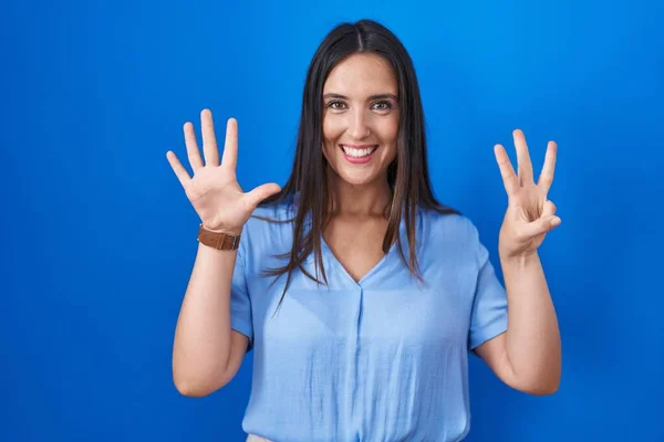 Genç Esmer Kadın Mavi Arka Planda Duruyor Sekiz Numaralı Parmaklarıyla — Stok fotoğraf