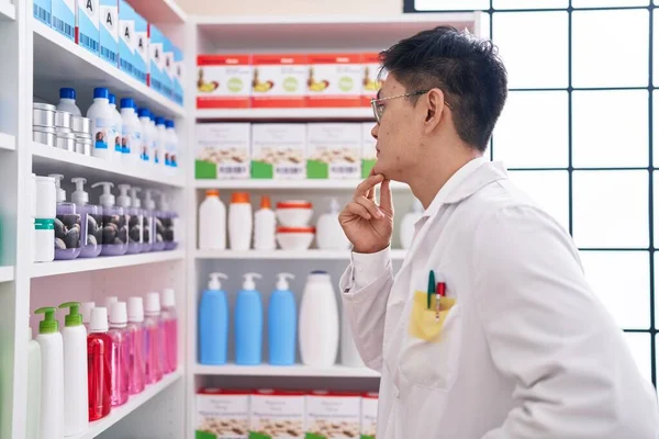 Young chinese man pharmacist looking product on shelving at pharmacy