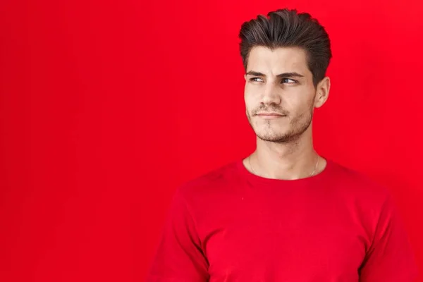 Young Hispanic Man Standing Red Background Smiling Looking Side Staring — Zdjęcie stockowe