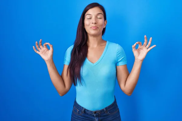 青い背景の上に立つ若いヒスパニック系の女性は 指で瞑想のジェスチャーを行う閉じて目でリラックスして笑顔 ヨガのコンセプト — ストック写真