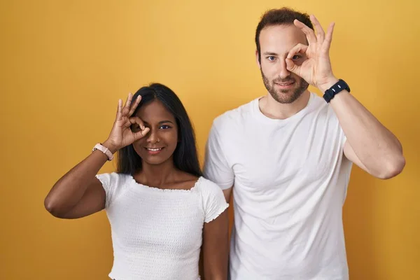 跨种族的夫妇站在黄种人的背景上 做着一个手势 面带微笑 用手指看过去 面带微笑 — 图库照片