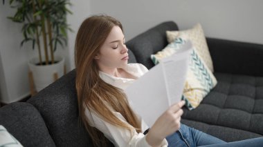 Young blonde woman using papers as a handfan suffering for hot at home