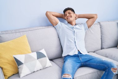 Genç İspanyol adam, ellerini başının üstüne koyup evinde kanepede oturarak rahatladı.