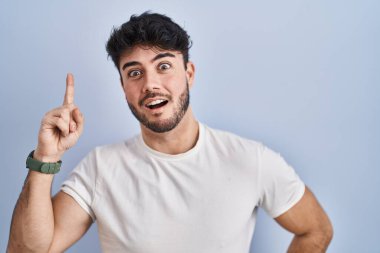 Hispanic man with beard standing over white background pointing finger up with successful idea. exited and happy. number one. 