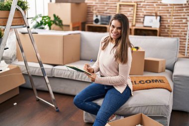 Genç, güzel, İspanyol bir kadın deftere yazı yazıyor. Yeni evindeki koltukta oturuyor.