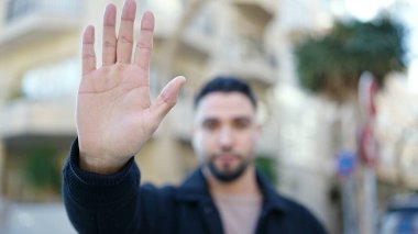 Genç Arap adam sokakta el hareketlerini durduruyor.