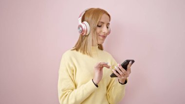 Young blonde woman listening to music dancing over isolated pink background