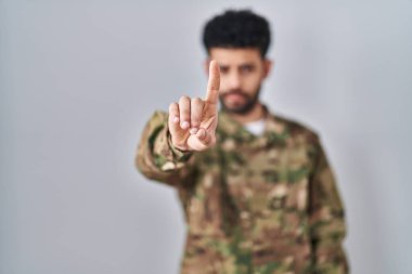 Arap adam kamuflaj üniforması giyip parmağını kaldırmış ve kızgın bir ifadeyle işaret ediyor. 
