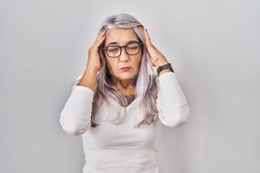 Beyaz arka planda beyaz saçlı orta yaşlı bir kadın elleri başının üstünde, stresten baş ağrısı çekiyor. migren ağrısı. 