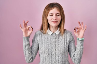 Beautiful woman standing over pink background relaxed and smiling with eyes closed doing meditation gesture with fingers. yoga concept. 
