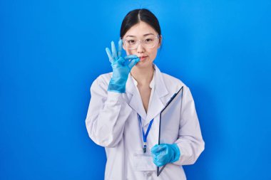 Chinese young woman working at scientist laboratory mouth and lips shut as zip with fingers. secret and silent, taboo talking 