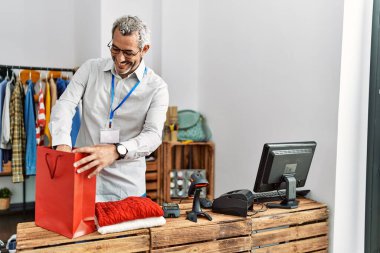 Orta yaşlı, gri saçlı bir dükkan asistanı giyim mağazasından alışveriş yapmaya hazırlanıyor.