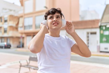 İkili olmayan adam sokakta durup müzik dinliyor.