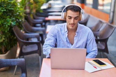 Latin asıllı genç bir adam kahve dükkanının terasında oturmuş video görüşmesi yapıyor.