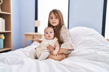 Erkek ve kız kardeş birbirlerine sarılıyorlar. Yatak odasında birlikte oturuyorlar.