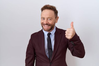 Middle age business man with beard wearing suit and tie doing happy thumbs up gesture with hand. approving expression looking at the camera showing success. 