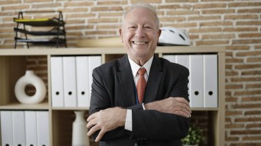 Ofiste çapraz kollarla duran üst düzey bir iş adamı.