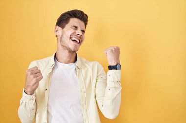 Young hispanic man standing over yellow background celebrating surprised and amazed for success with arms raised and eyes closed. winner concept. 