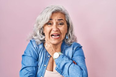 Middle age woman with grey hair standing over pink background shouting suffocate because painful strangle. health problem. asphyxiate and suicide concept. 