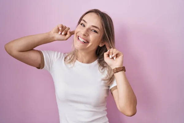 Blonde Caucasian Woman Standing Pink Background Smiling Pulling Ears Fingers —  Fotos de Stock