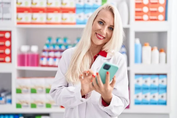 Young Blonde Woman Pharmacist Using Smartphone Working Pharmacy — Foto Stock